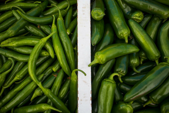 Two varieties of organic green chili peppers - Jalapeño and Serrano, in a box at a market in California