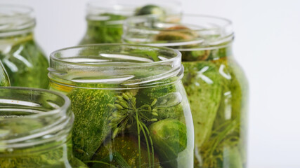 Close-up glass jars filled with fresh cucumbers,dill,garlic and black pepper and poured with brine white background.Canning,pickling fermenting vegetables.Homemade pickling cucumber recipes.Copy space
