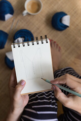 Closeup view of a woman with well cared nails drawing a design with a pencil on a spiral notebook.