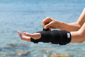 A woman on a seaside vacation puts on an orthopedic brace on her injured arm.