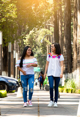 Two young Mexican women, walking on a sidewalk