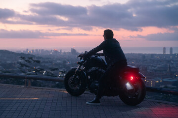 Silhouette portrait of biker or moto rider before sunrise, doing his trip ride with beautiful city views at background