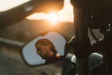 Fototapeta na wymiar Handsome biker looking away through mirror of his motorcycle