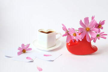 Obraz na płótnie Canvas The concept of a good morning. Delicate pink flowers in a red heart-shaped vase, a cup of hot coffee on a light background, a light background, a side view, a place for text
