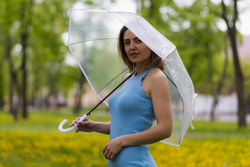 Young woman with transparent umbrella on blurred background of city park. Copy space