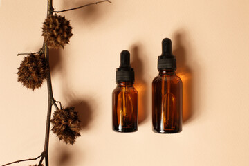 Dropper glass bottles mock up with dry flowers. Skincare brown bottle container on pastel pink background. Natural organic beauty product concept. Minimalism style. Flat lay.