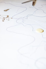 Macro close-up of colored threads next to scissors, threader, button, needles and safety pins, against white background