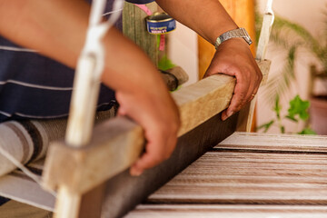 Closeup of hand of a craftsman weaving a tapestry on a wooden loom
