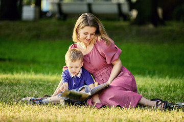 Naklejka na ściany i meble Mother and child lie on grass and read book outdoors.