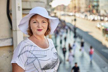 Old woman in white hat walks in city center.