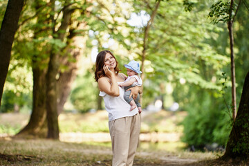 Woman holds little child and talks by cell phone outdoors.