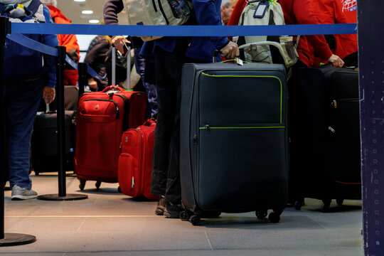 Group Of People With Luggage Lining Up At An Airport Check-in Counter