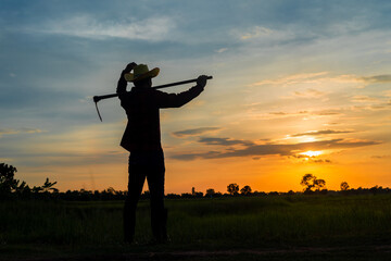 Fototapeta na wymiar Male farmer holding a hoe in a field at sunset