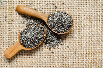 A couple of dry organic chia seed pile in small wooden spoon on brown sack fabric background. For natural and healthy food ingredient or agricultural product concept