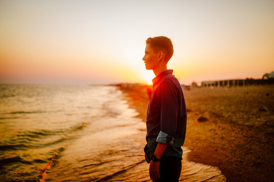 A woman of androgynous appearance looks at the sea at sunset