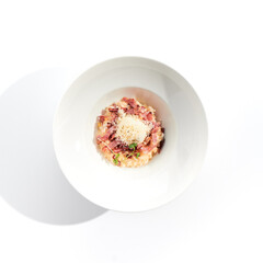 Risotto alla carbonara on white restaurant plate. Risotto with bacon and egg, garnished with micro greens. Risotto topped with parmesan cheese.