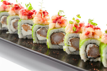 Shrimp Sushi Roll on black slate plate. Luxury maki sushi roll with cream cheese and shrimp inside. Seafood sushi roll topped with spicy scallop. Isolated on white background.