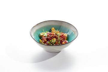 Tuna and cucumber salad bowl. Blue salad bowl isolated on white background. Salad garnished with micro greens and sesame, chopped tuna, sliced cucumber and parsley green leaf