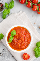 Traditional Italian marinara sauce in a bowl on a concrete background with spices and ingredients. Top view. Copy space.