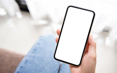 Mockup woman hand holding the black smart phone with blank white screen on sofa at home. Business and technology concept