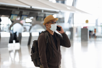 Young traveler man wearing mask to protect flu coronavirus Covid-19. Tourist in airport terminal using smartphone check in at counter. Nobody in terminal.