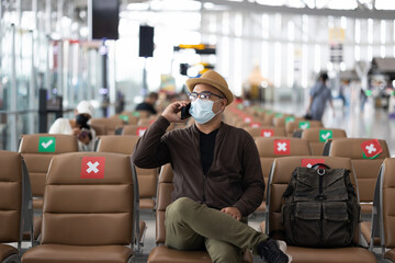Young traveler man wearing mask protect flu coronavirus. Tourist in airport terminal using smartphone sitting and waiting his flight. During the pandemic must be social distancing self quarantine.