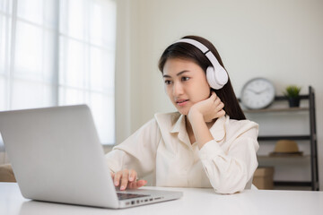 Young asian woman in headphone using laptop chatting video conference online sitting in living room at home. Business Woman look at screen Meeting on social live steam. Work, learning from home.