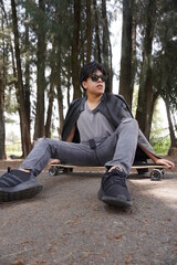 Obraz premium Full shot of a young man. He is sitting on his longboard and is wearing sunglasses and streetwear.