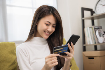 Fototapeta na wymiar Shopping online. Young asian teenage girl input the serial number of credit card to smartphone for shopping payment. Buy item online delivery at home. Smiling female feeling happy.