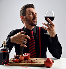 Stylish man expert, sommelier in black shirt with striped tie and suspenders sits at table with...