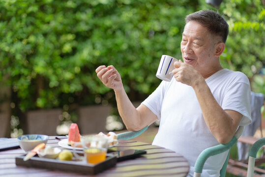 portrait of senior retired asian man eating healthy breakfast and drinking coffee in garden