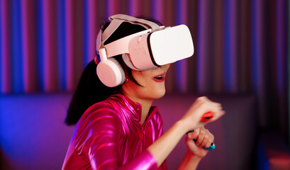 Young asian woman is using virtual reality headset. Neon light studio portrait. Concept of virtual reality, simulation, gaming and future technology.Asian woman play game in bedroom.