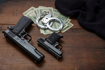 Pistol handcuffs and American dollar banknotes on black background.