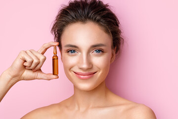Woman holds ampoule with serum for hair or skin care. Photo of attractive woman with perfect makeup on pink background. Beauty concept - obrazy, fototapety, plakaty