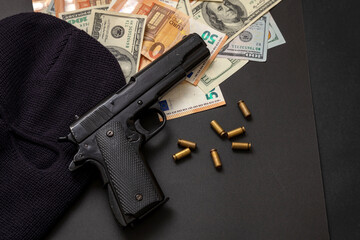 Pistol and balaclava on dollar and euro banknotes, black background
