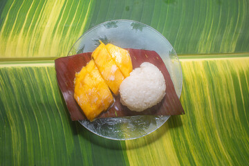 .Mango sticky rice served on a spotted banana leaf by the pool..speckled banana leaves in the...