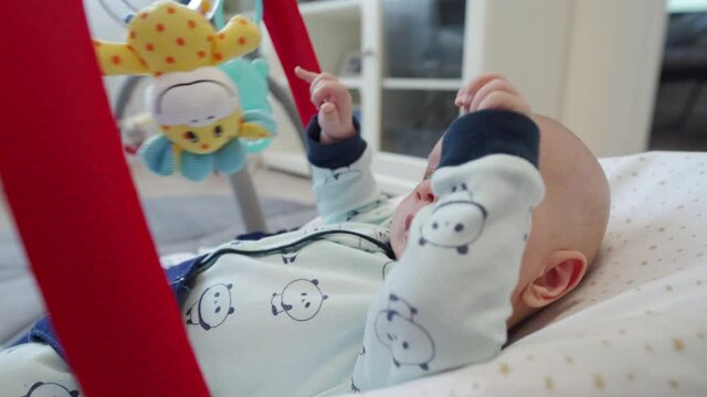 2 month old baby boy in bouncer for babies, infant playing with hanging toys. High quality 4k footage