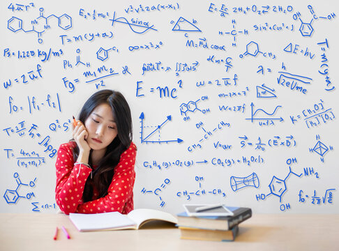Young beautiful college student reading a book with chemical formulas and mathematical equations on her background