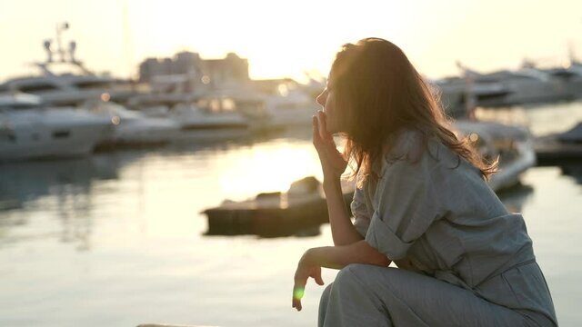 portrait of a woman sitting on the beach with yachts on the background in the rays of the setting sun and sad