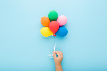 Baby boy hand holding heap of colorful balloons on light blue table background. Pastel color. Closeup. Top down view.