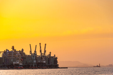 Dock industry cranes silhouette in container terminal port with golden sunset sky with clouds