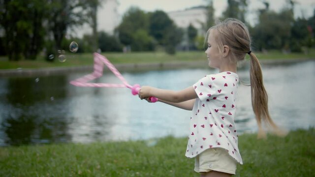 Little girl with cheerful smile making very big bubbles outdoors. Young girl playing outdoors