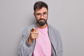 Self assured serious man with beard points index finger at camera chooses you looks directly at...