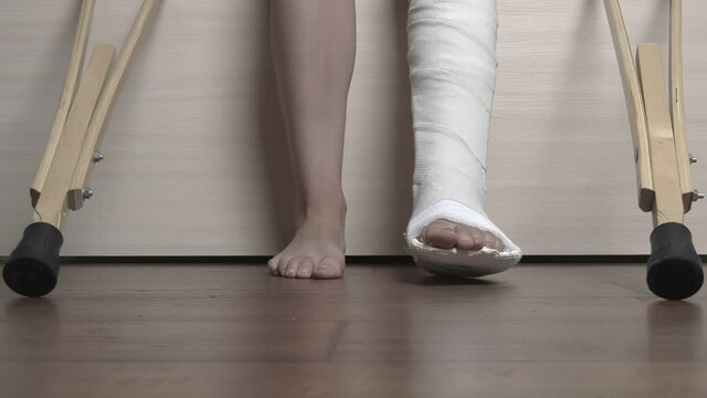 Woman with a broken leg in a plaster cast gets out of bed and walks around the room on crutches. High quality FullHD footage. 50FPS, downscaling.