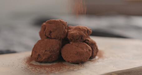 sprinkle cocoa powder over handmade chocolate truffles on a wood board