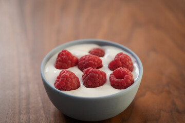 Yogurt with fresh raspberries in blue ceramic bowl on walnut table