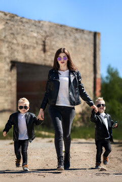 Mom goes by the hand with her sons.Mother and twins on the background of an abandoned building.A bold image of a family look for a photo shoot.The family is dressed in leather jackets.Idea for a photo