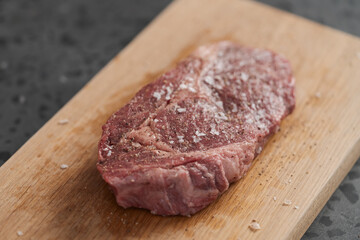 Raw ribeye steak spiced and ready to cook on oak board