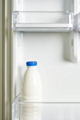 A bottle of sour cream in refrigerator. Yogurt in white bottle on shelf of open empty fridge. Weight loss diet concept. Fermented food