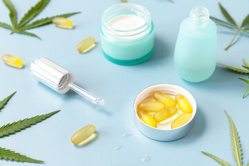 Herbal Alternative Medicine Concept, cosmetics CBD oil. Cannabis leaf skincare cosmetic product. Moisturizing cream, Serum, capsules oil on a pastel blue background.
